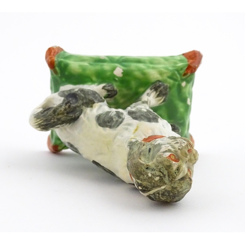 56 - A 19thC model of a seated dog with a red collar on a green tasselled cushion. Approx. 3 3/4