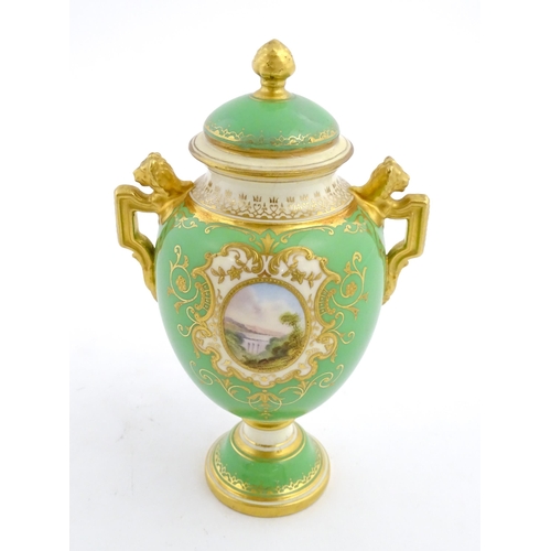 85 - A Coalport urn and cover with twin lion head handles, the green ground decorated with hand painted v... 