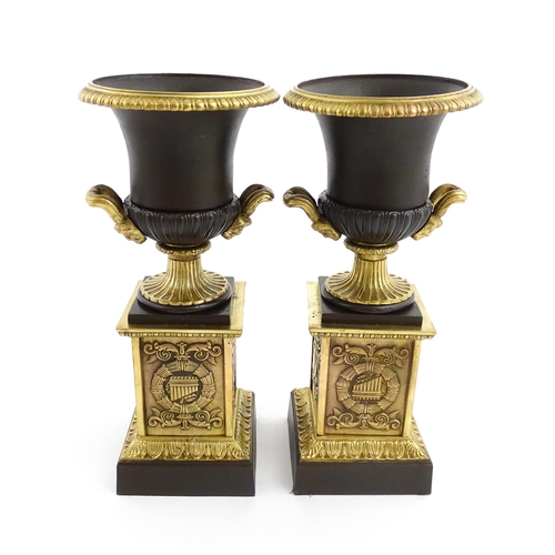 1019 - A pair of cast bronze campana urns with twin handles raised on squared plinths with relief symbols o... 