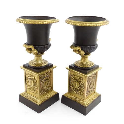 1019 - A pair of cast bronze campana urns with twin handles raised on squared plinths with relief symbols o... 