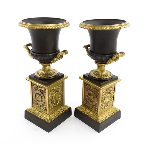 1019 - A pair of cast bronze campana urns with twin handles raised on squared plinths with relief symbols o... 