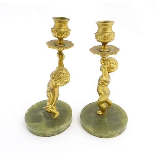 1020 - A pair of 20thC gilt metal candlesticks formed as cherubs holding aloft a sconce, on an onyx base. A... 