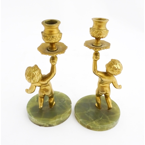 1020 - A pair of 20thC gilt metal candlesticks formed as cherubs holding aloft a sconce, on an onyx base. A... 