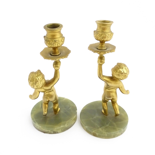 1020 - A pair of 20thC gilt metal candlesticks formed as cherubs holding aloft a sconce, on an onyx base. A... 