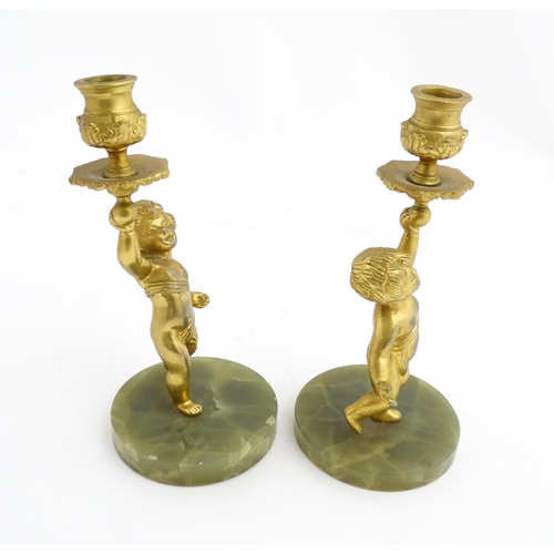 1020 - A pair of 20thC gilt metal candlesticks formed as cherubs holding aloft a sconce, on an onyx base. A... 