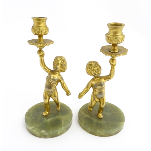 1020 - A pair of 20thC gilt metal candlesticks formed as cherubs holding aloft a sconce, on an onyx base. A... 