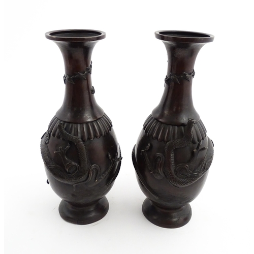 1041 - A pair of Chinese cast vases with flared rims decorated with relief dragon decoration, the necks wit... 