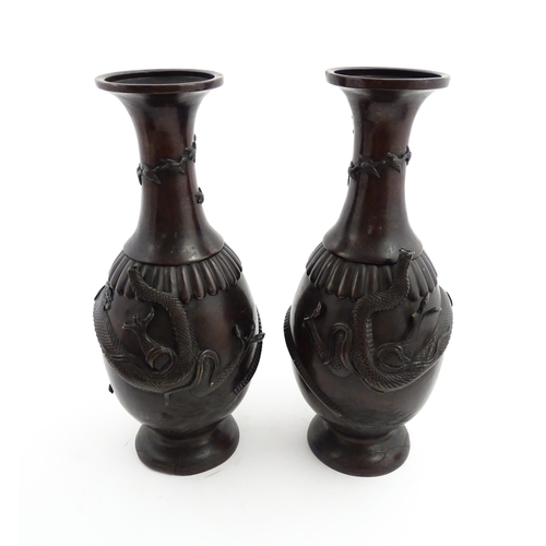 1041 - A pair of Chinese cast vases with flared rims decorated with relief dragon decoration, the necks wit... 