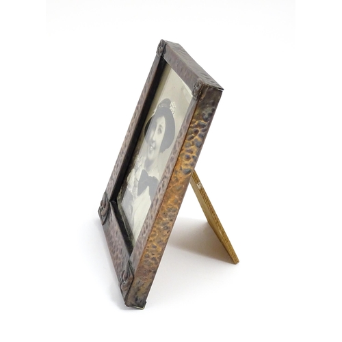 1004 - An Arts & Crafts style easel back photograph frame of tapering form with hammered copper surround an... 