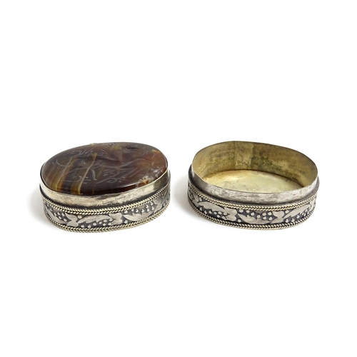 1040 - A white metal pill box of oval form with banded decoration, the top set with agate intaglio depictin... 