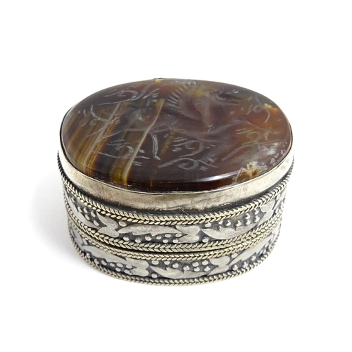 1040 - A white metal pill box of oval form with banded decoration, the top set with agate intaglio depictin... 