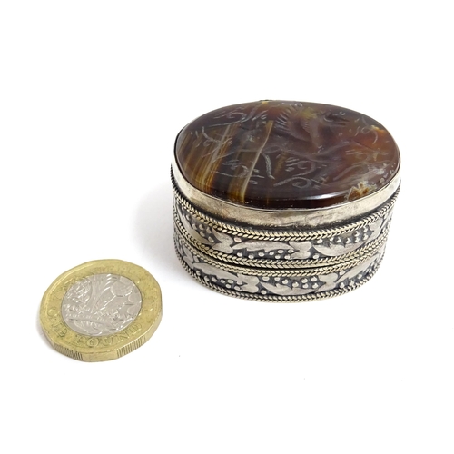 1040 - A white metal pill box of oval form with banded decoration, the top set with agate intaglio depictin... 