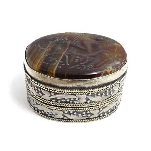 1040 - A white metal pill box of oval form with banded decoration, the top set with agate intaglio depictin... 