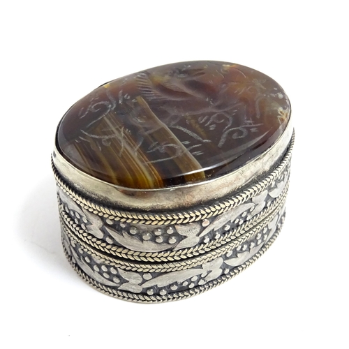 1040 - A white metal pill box of oval form with banded decoration, the top set with agate intaglio depictin... 