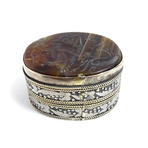 1040 - A white metal pill box of oval form with banded decoration, the top set with agate intaglio depictin... 