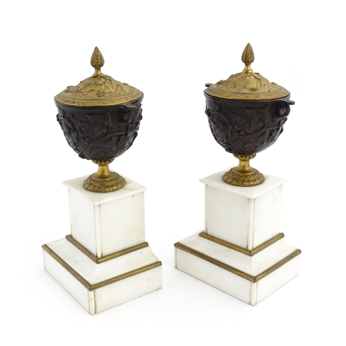 1059 - A pair of late 19th / early 20thC cast lidded urns with scrolling vine decoration, each raised on a ... 