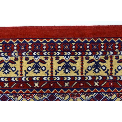 1385 - Carpet / Rug : A red ground rug decorated with repeating floral and geometric motifs. Approx. 79