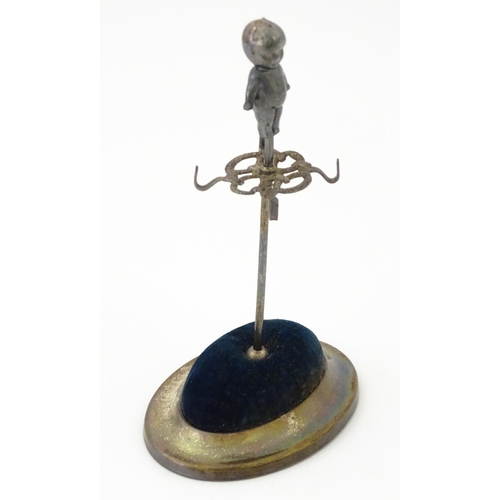 334 - A silver plate hat pin holder / ring tree surmounted by a model of a Kewpie doll. Marked with regist... 