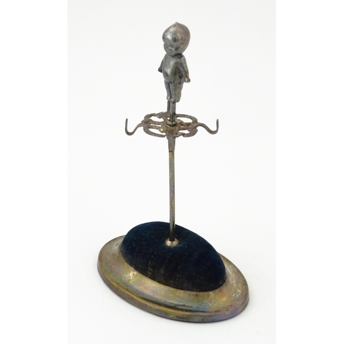 334 - A silver plate hat pin holder / ring tree surmounted by a model of a Kewpie doll. Marked with regist... 