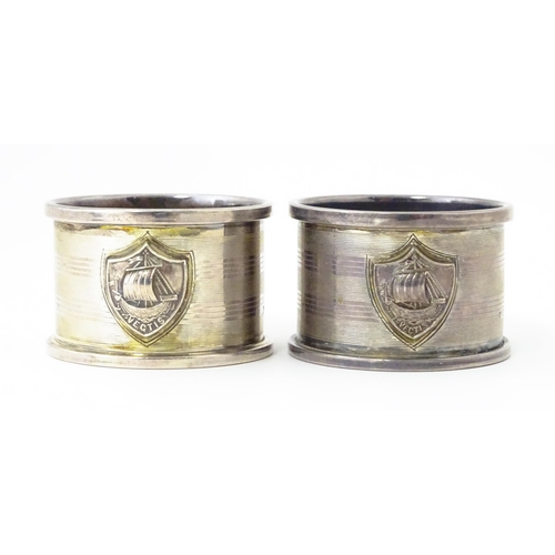 379 - A pair of Art Deco silver napkin rings with engine turned decoration and shield crest depicting boat... 