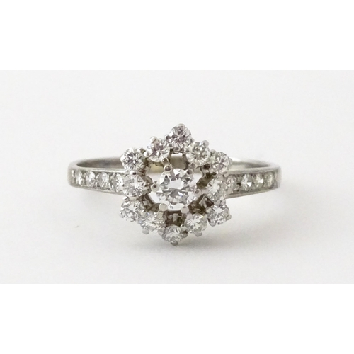 603 - A white gold ring set with diamonds in a daisy setting flanked by further diamonds to shoulders. Rin... 