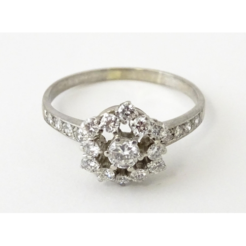 603 - A white gold ring set with diamonds in a daisy setting flanked by further diamonds to shoulders. Rin... 