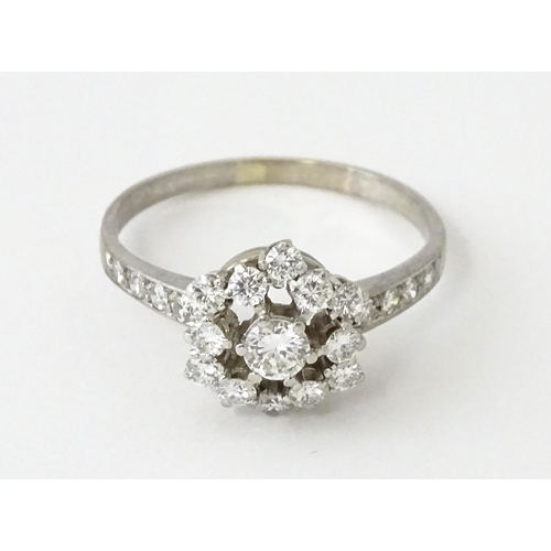 603 - A white gold ring set with diamonds in a daisy setting flanked by further diamonds to shoulders. Rin... 