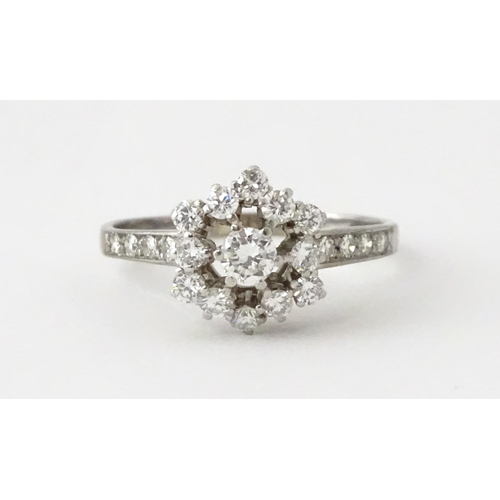 603 - A white gold ring set with diamonds in a daisy setting flanked by further diamonds to shoulders. Rin... 