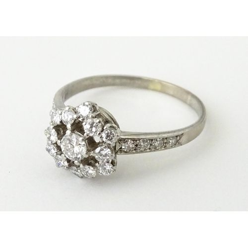 603 - A white gold ring set with diamonds in a daisy setting flanked by further diamonds to shoulders. Rin... 