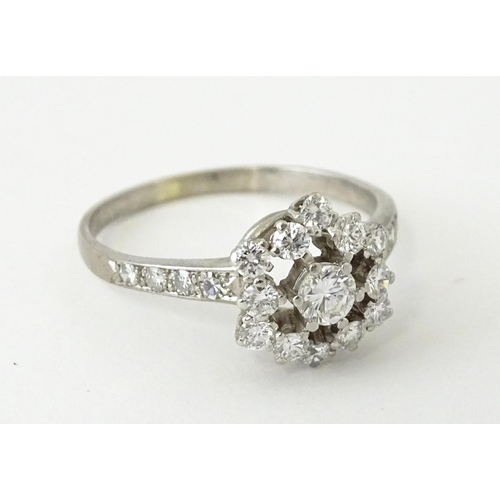 603 - A white gold ring set with diamonds in a daisy setting flanked by further diamonds to shoulders. Rin... 