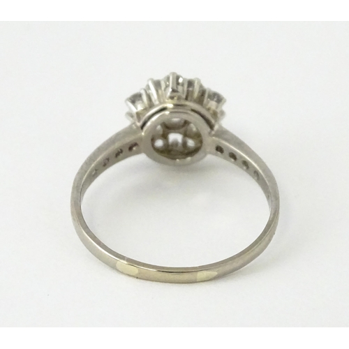 603 - A white gold ring set with diamonds in a daisy setting flanked by further diamonds to shoulders. Rin... 