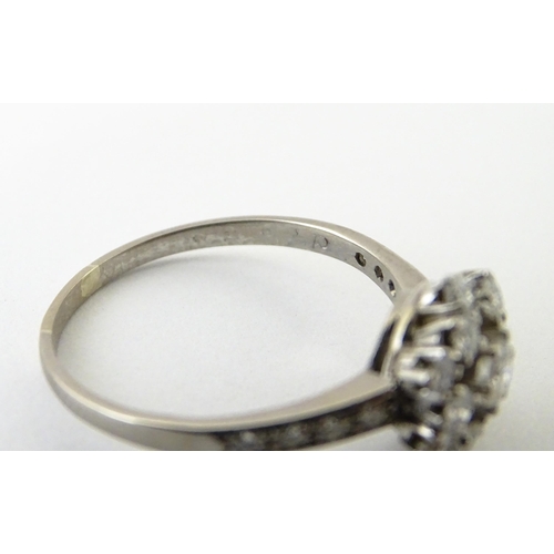 603 - A white gold ring set with diamonds in a daisy setting flanked by further diamonds to shoulders. Rin... 