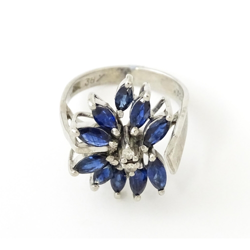 636 - A white metal dress ring set with a profusion of sapphires and two central diamonds in a stylised fl... 