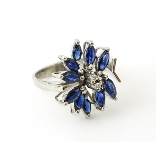 636 - A white metal dress ring set with a profusion of sapphires and two central diamonds in a stylised fl... 