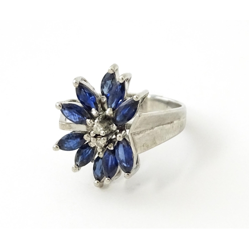 636 - A white metal dress ring set with a profusion of sapphires and two central diamonds in a stylised fl... 