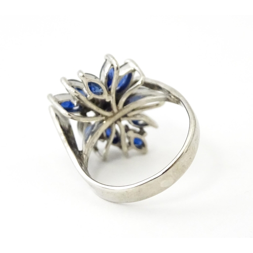 636 - A white metal dress ring set with a profusion of sapphires and two central diamonds in a stylised fl... 