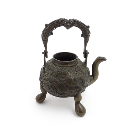 1035A - A Chinese brass miniature teapot with swing handle and raised on three feet, the body with relief de... 