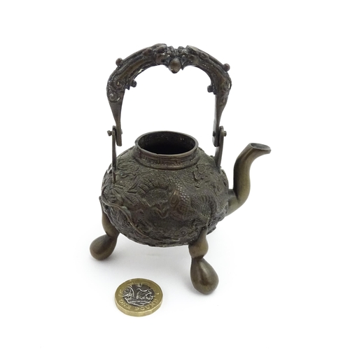 1035A - A Chinese brass miniature teapot with swing handle and raised on three feet, the body with relief de... 