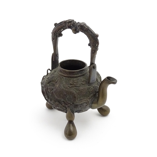 1035A - A Chinese brass miniature teapot with swing handle and raised on three feet, the body with relief de... 