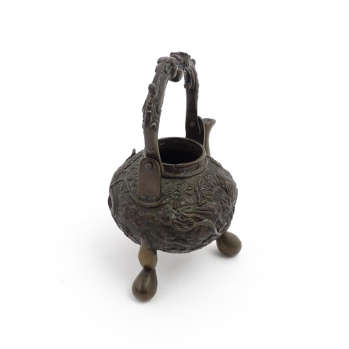 1035A - A Chinese brass miniature teapot with swing handle and raised on three feet, the body with relief de... 