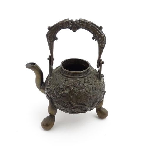 1035A - A Chinese brass miniature teapot with swing handle and raised on three feet, the body with relief de... 