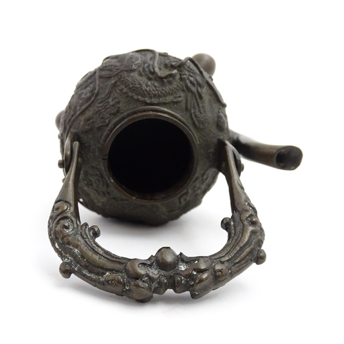 1035A - A Chinese brass miniature teapot with swing handle and raised on three feet, the body with relief de... 