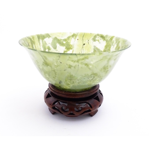 1037 - A Chinese jade coloured bowl with flared rim, on a carved wooden stand. Approx. 3 1/2