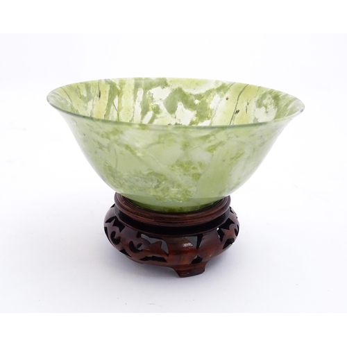 1037 - A Chinese jade coloured bowl with flared rim, on a carved wooden stand. Approx. 3 1/2