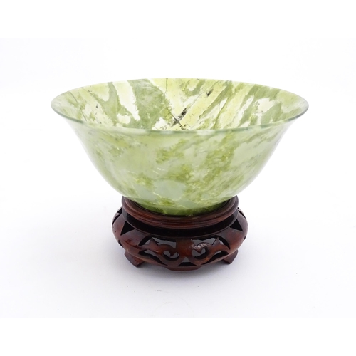 1037 - A Chinese jade coloured bowl with flared rim, on a carved wooden stand. Approx. 3 1/2