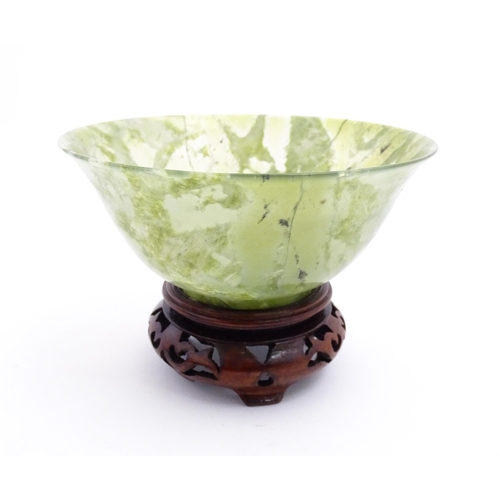 1037 - A Chinese jade coloured bowl with flared rim, on a carved wooden stand. Approx. 3 1/2