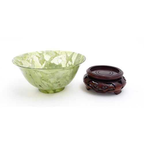 1037 - A Chinese jade coloured bowl with flared rim, on a carved wooden stand. Approx. 3 1/2