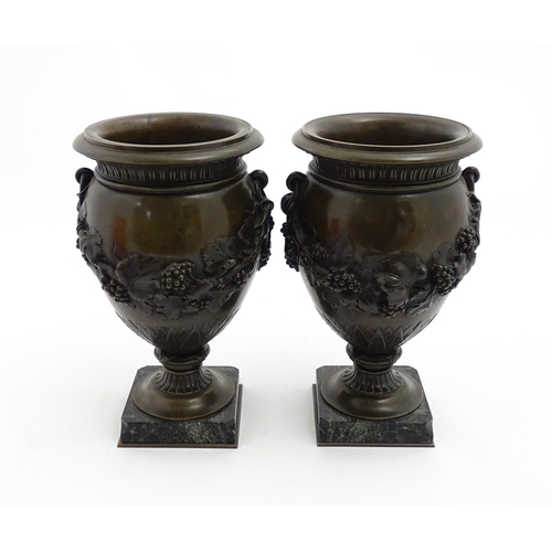 1225 - A pair cast pedestal urns with twin handles and relief fruiting vine decoration, raised on a marble ... 