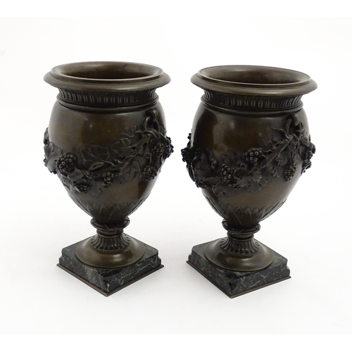 1225 - A pair cast pedestal urns with twin handles and relief fruiting vine decoration, raised on a marble ... 