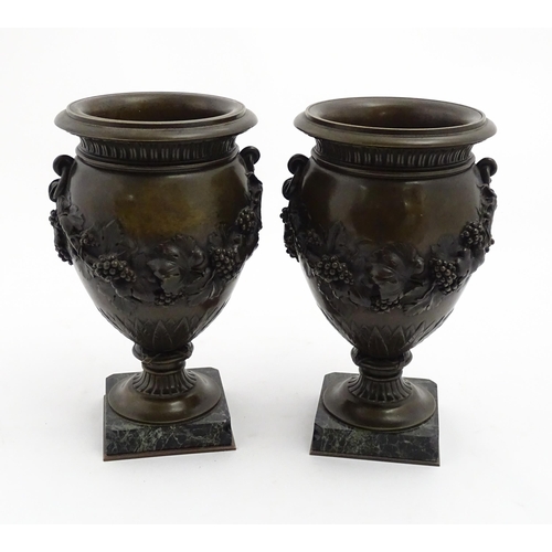 1225 - A pair cast pedestal urns with twin handles and relief fruiting vine decoration, raised on a marble ... 